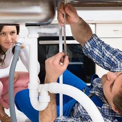 a homeowner watches as her husband attempts to fix their sink